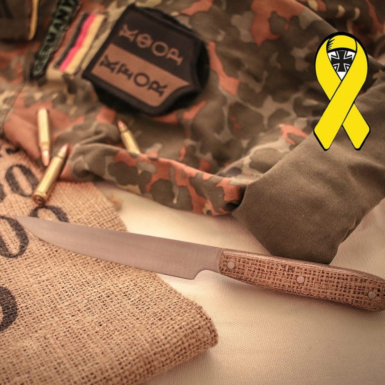 Steakmesser mit Griff aus Sandsack Mikarta Küchenmesser auf einer Juteunterlage, umgeben von Tarnkleidung und Patronen.