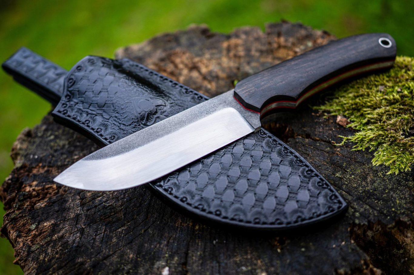 Hochwertiges Bushcraftmesser mit handgenähter Scheide Ein großes Bushcraftmesser mit dunkler Klinge und schwarzer Lederscheide auf einem Baumstumpf.