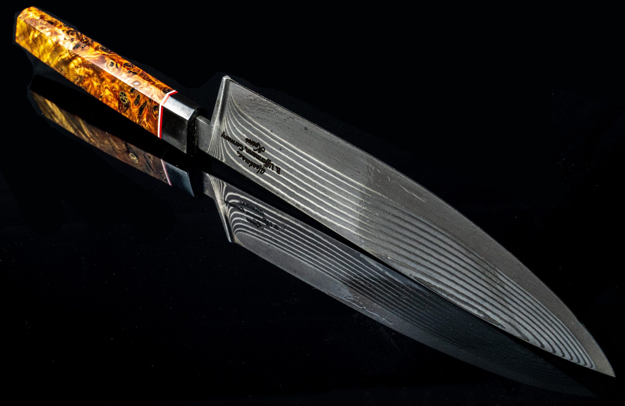 Damast Chefmesser Kochmesser mit glänzender Damastklinge und orangefarbenem Griff auf schwarzem Hintergrund.